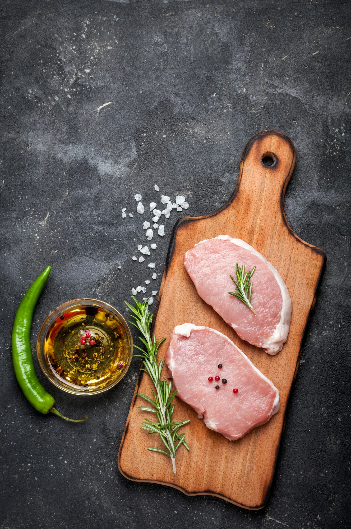 Raw meat with herbs, oil and spices on dark background with copy space. Raw pork steak